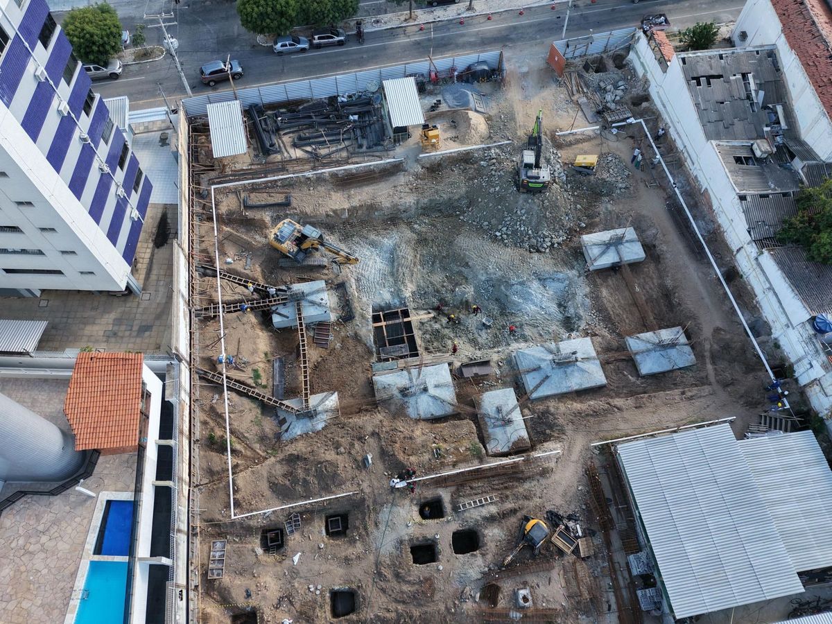 Vista de drone, de cima, das sapatas de fundação concretadas e de escavadeiras no terreno.