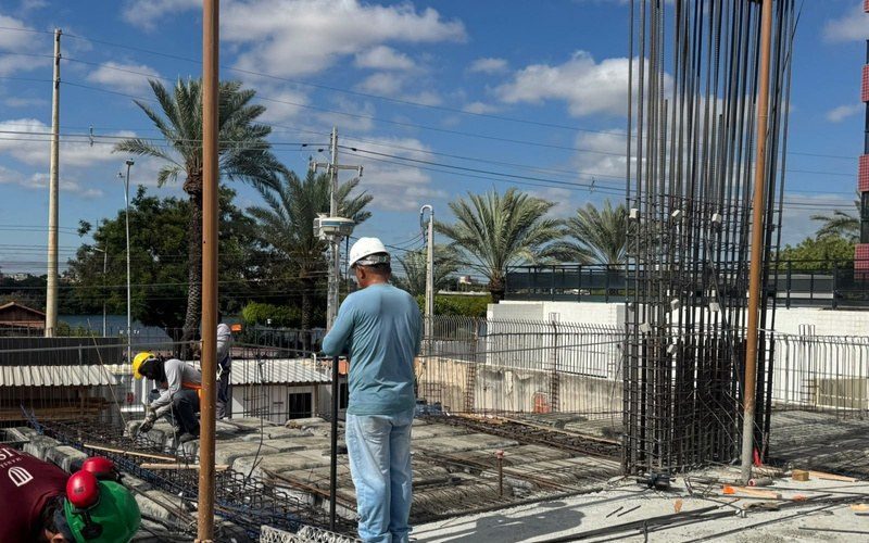 Profissional de topografia com estação total, entre as armaduras dos pilares.
