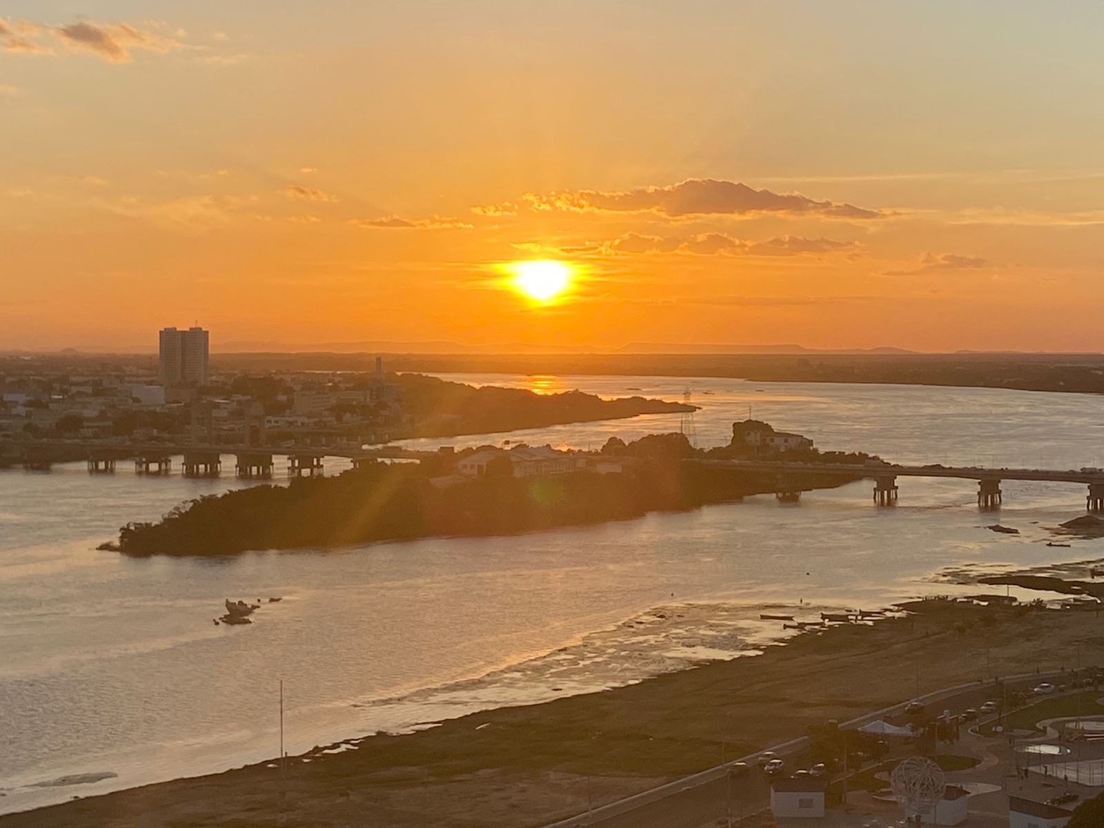 Entardecer na orla de Petrolina: o Rio São Francisco em tons dourados, a ilha, a ponte e a cidade ao fundo.